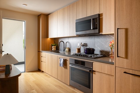 A modern kitchen with wooden cabinets and a black microwave above the stove.