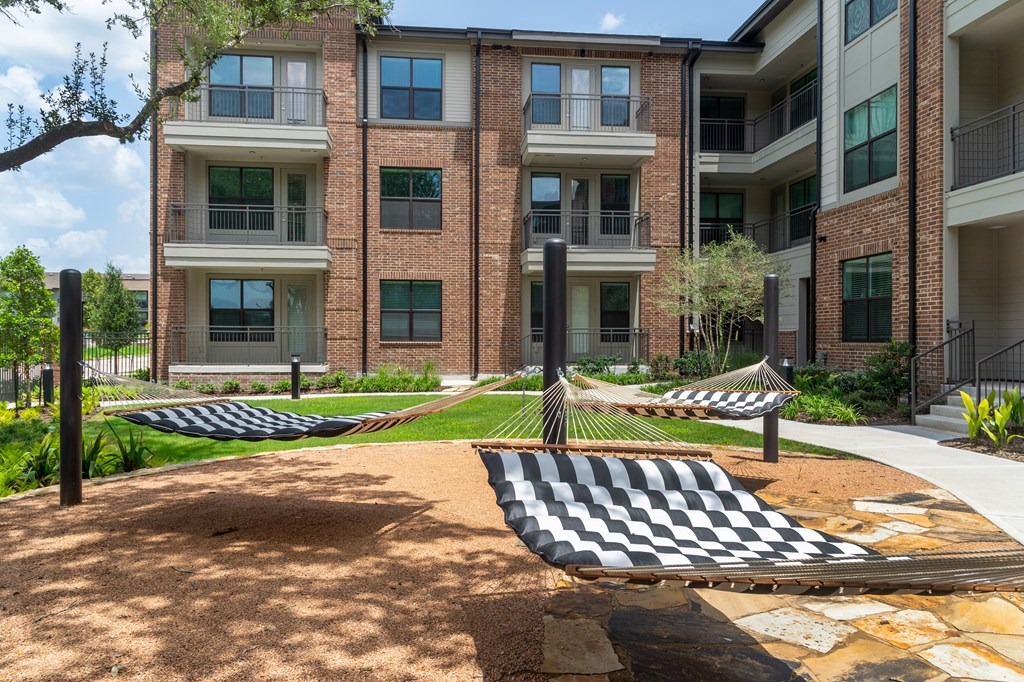 A black and white checkered hammock is in the foreground of a courtyard with a brick building in the background.