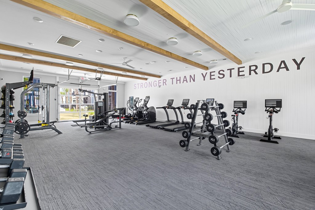 A gym with a variety of equipment and a sign that says "STRONGER THAN YESTERDAY".