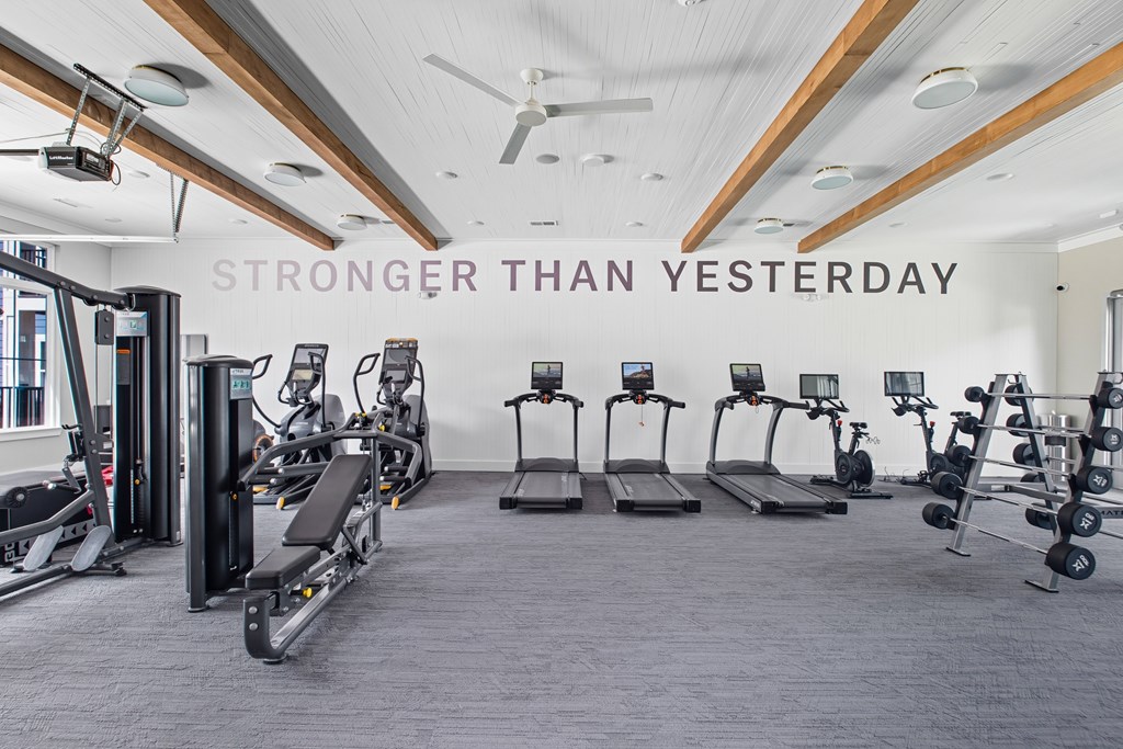 A gym with a variety of equipment and a sign that says "STRONGER THAN YESTERDAY".