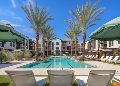 A pool surrounded by palm trees and lounge chairs.