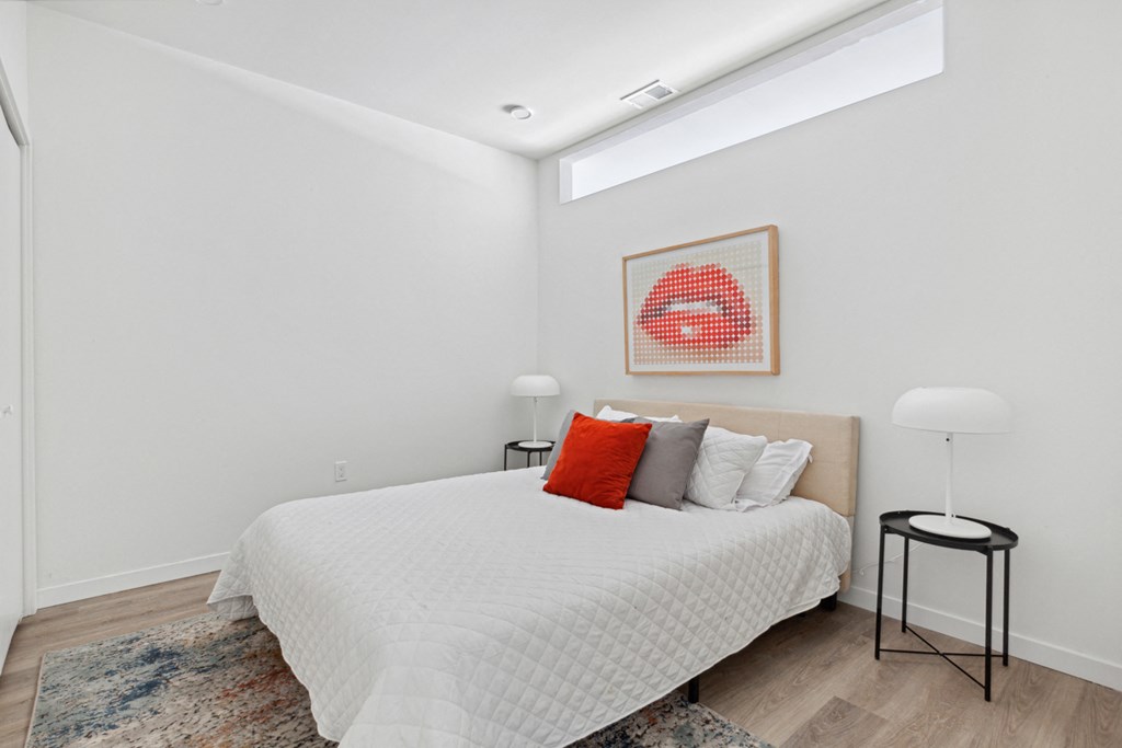 a bedroom with white walls and a white bed with red and gray pillows