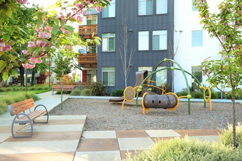 A playground with a slide, swings, and a bench in front of a building.