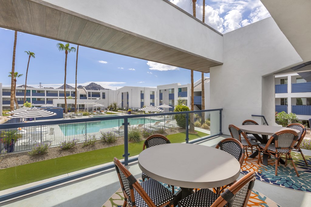A patio with a table and chairs overlooks a pool and a building.
