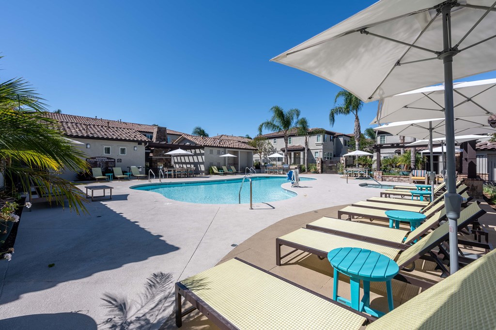 a swimming pool with lounge chairs and umbrellas in a resort style pool area