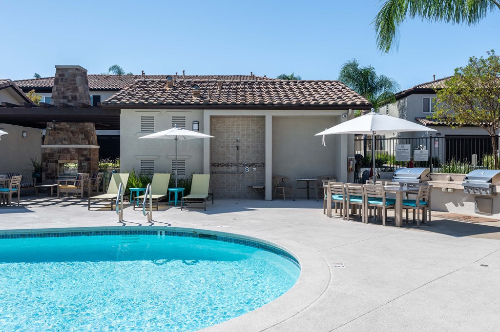 a swimming pool in front of a house with tables and umbrellas
