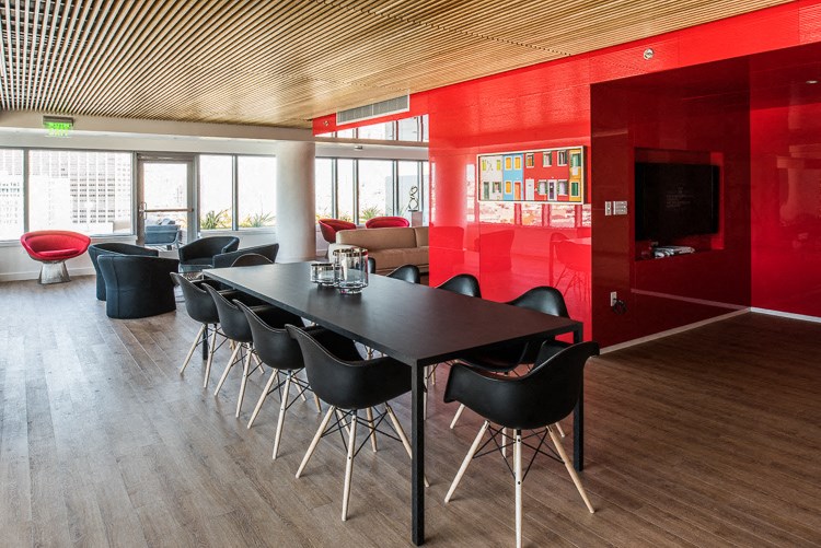 a room with a long black table with black chairs and a red wall with a television in