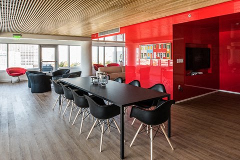 a room with a long black table with black chairs and a red wall with a television in