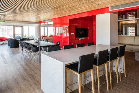 Studios in San Francisco CA - Trinity Place at 33 8th - Clubhouse Lounge Space with Red Accent Walls, TV, Couches, Tables with Chair, and City Views Through Large Windows