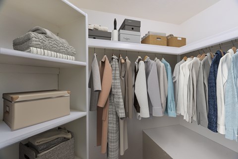 A white closet with clothes hanging and folded items on shelves.