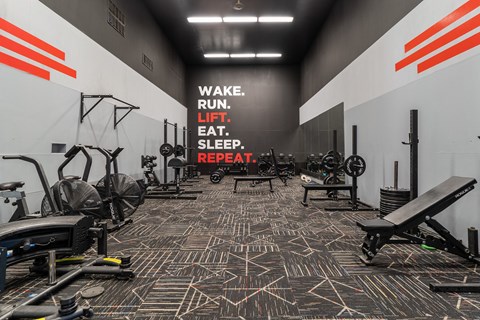 a workout room with weights and cardio machines and a motivational wall in the background