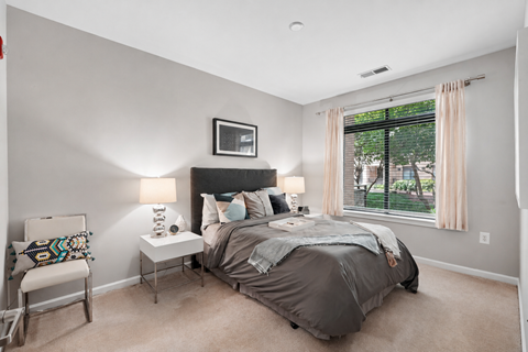 A bedroom with a bed, nightstand, chair, and window.