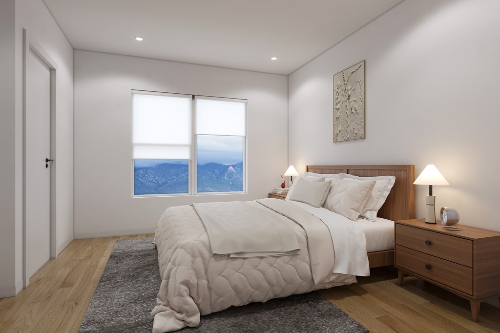 A bedroom with a large bed, a nightstand with a lamp, and a window with a view of the mountains.
