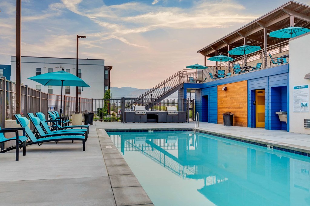 a swimming pool with blue chairs and umbrellas at a building with a pool