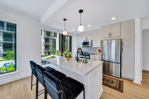 A kitchen with a white quartz countertop and black bar stools. Stainless steel appliances and large windows. 113 Potomac Ave SW Washington, DC 20024