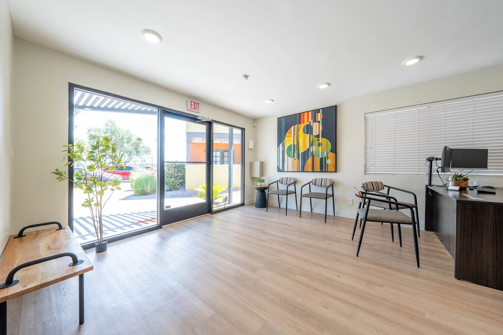 a room with a desk and chairs and a sliding glass door with a view of a courtyard