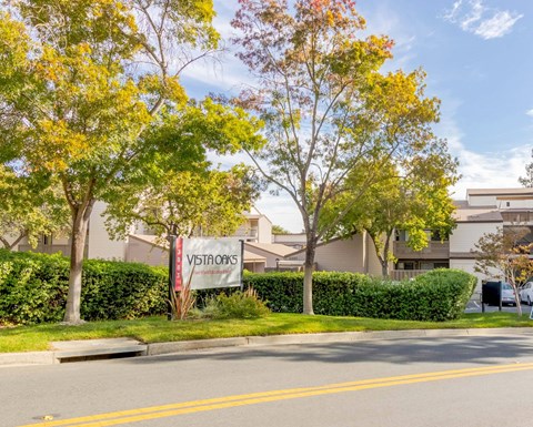 A Vista Oaks sign is displayed on a tree in front of a row of houses.