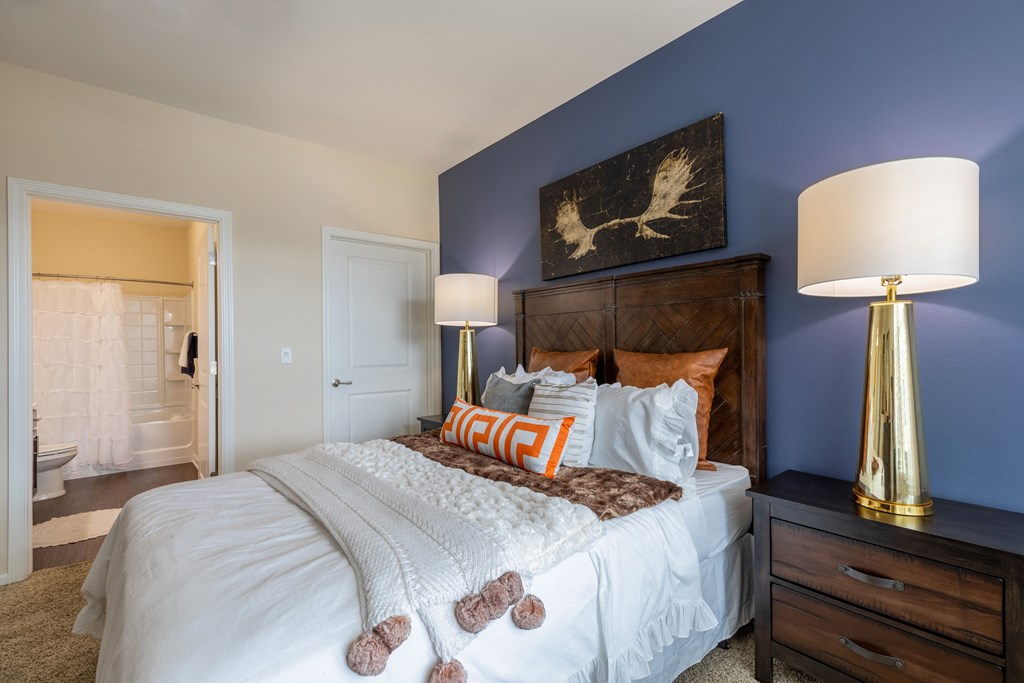 bedroom with blue accent wall and white bed with pillows and orange pillows on