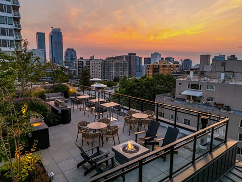 a rooftop terrace with tables and chairs overlooking the city at sunset