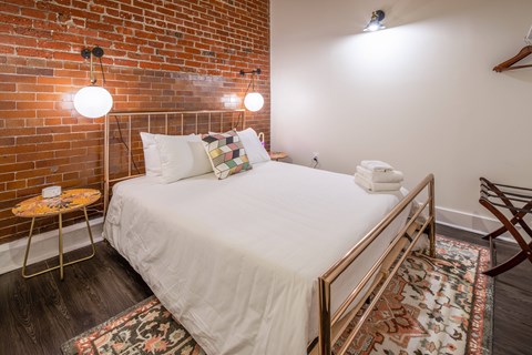 A bedroom with a white bed and a brick wall.