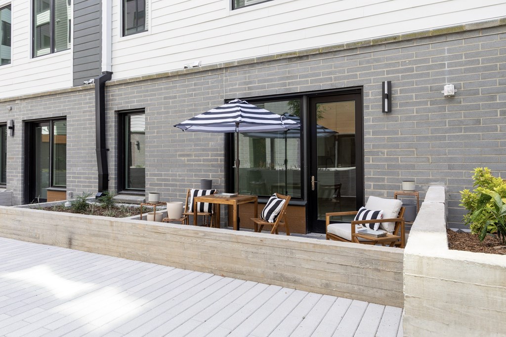 A modern house with a striped umbrella over a wooden chair.