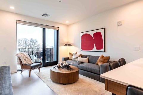 A modern living room with a large window and a red abstract painting on the wall.