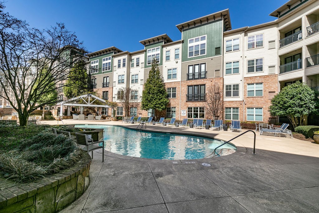 a swimming pool with chaise lounge chairs and trees in front of an apartment building at Westmount at Ashwood, Atlanta, GA, 30338