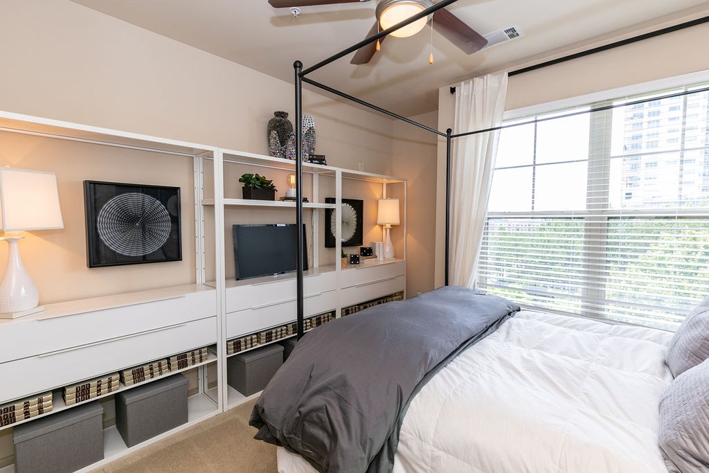 A bedroom with a bed, a fan, and a window with blinds.