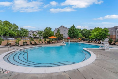 A large outdoor swimming pool with a white lounge chair and orange umbrella.