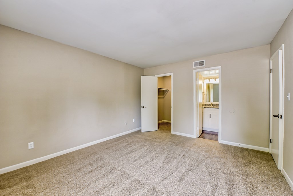 a bedroom with a carpeted floor and an open doorway to a bathroom
