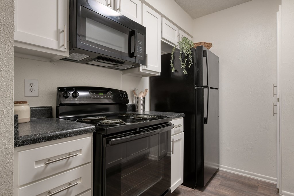 A black refrigerator stands in a kitchen with white cabinets and a black stove.