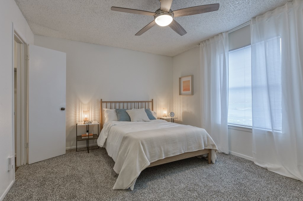 A bedroom with a bed, carpet, and a ceiling fan.