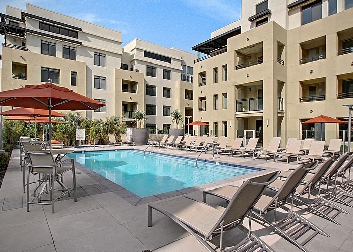 a swimming pool with chaise lounge chairs and umbrellas in front of an apartment building