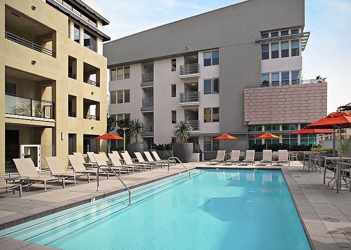 a swimming pool with chaise lounge chairs and umbrellas in front of a building