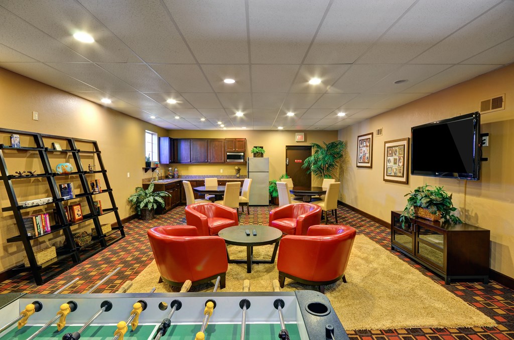A foosball table is in the middle of a room with red chairs and a bookshelf.
