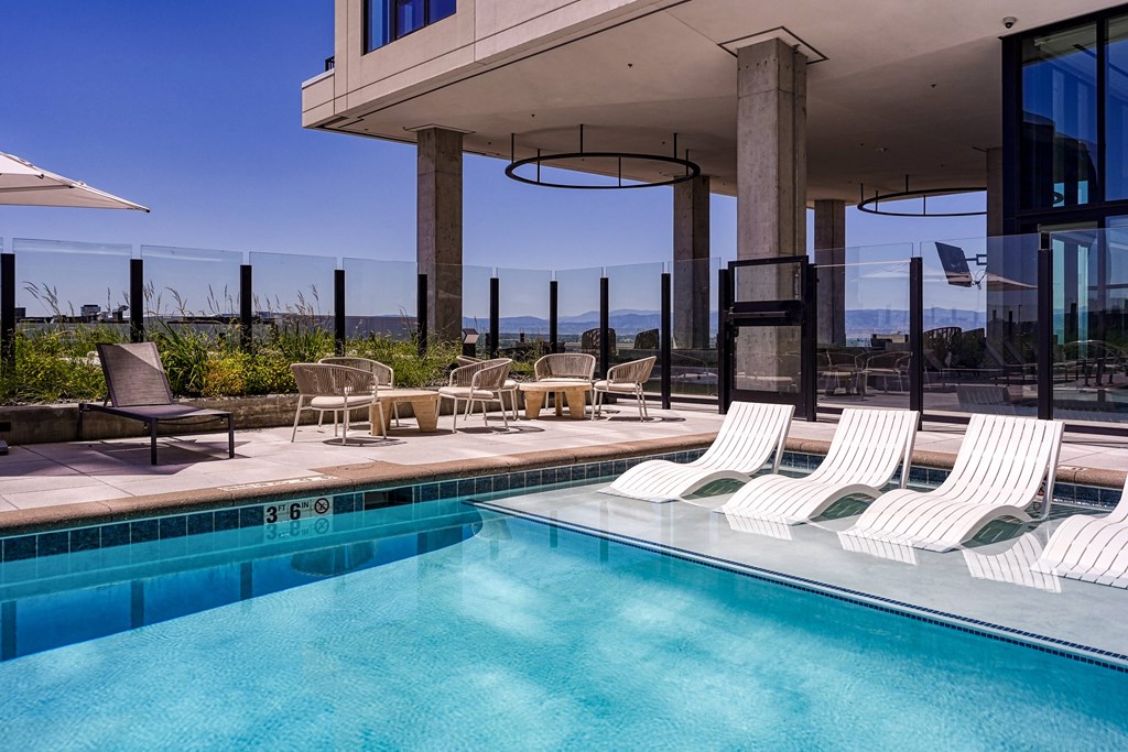 a swimming pool with white lounge chairs next to a building with glass doors