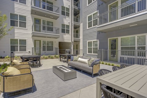 A patio area with furniture and a fire pit in front of apartment buildings.