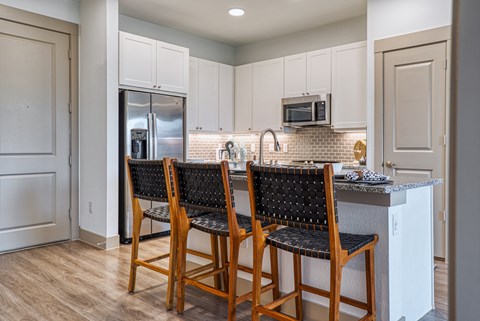 a kitchen with white cabinets and a island with three chairs