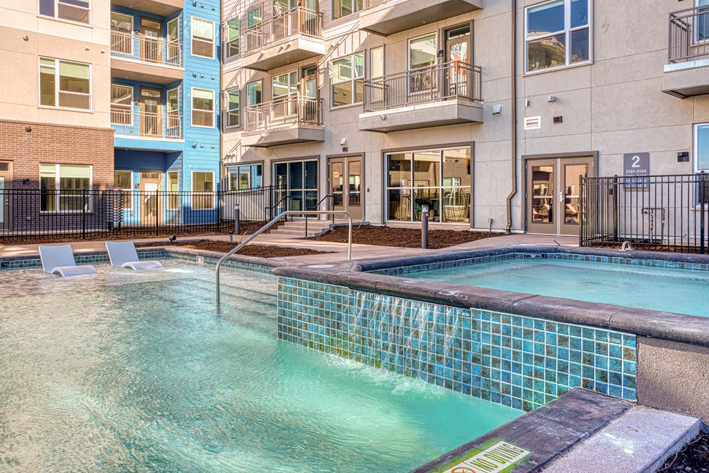 a swimming pool in front of an apartment building with a hot tub