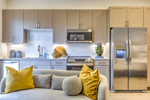 A modern kitchen with a grey couch and yellow pillows.