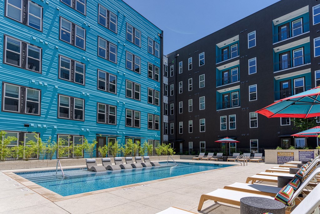 an outdoor pool with lounge chairs and umbrellas in front of a blue and black building