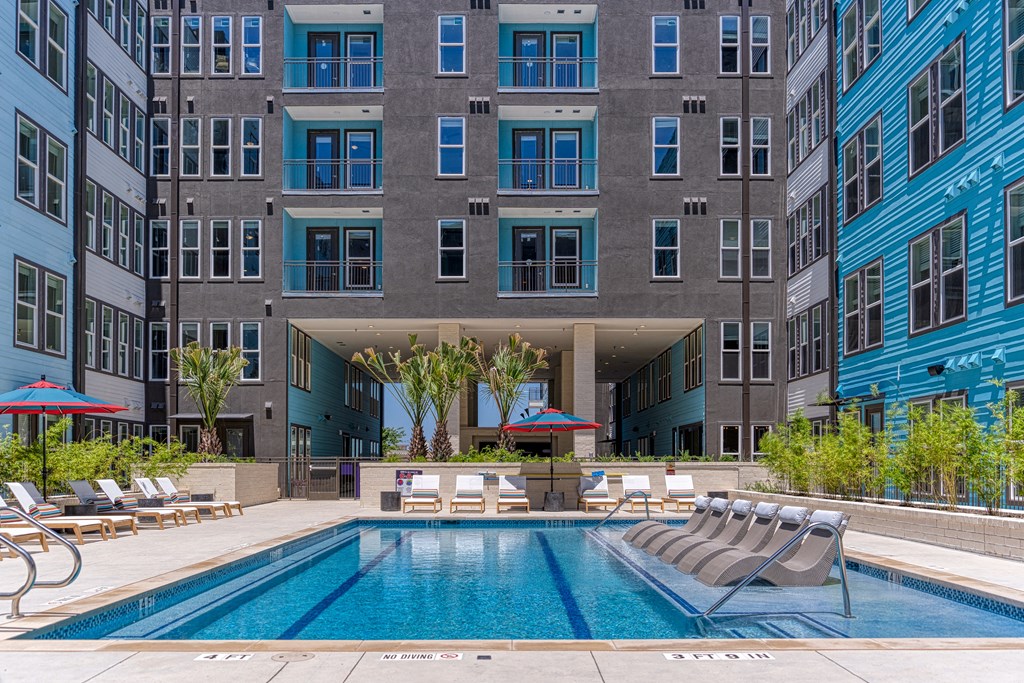 a pool with lounge chairs and umbrellas in front of an apartment building