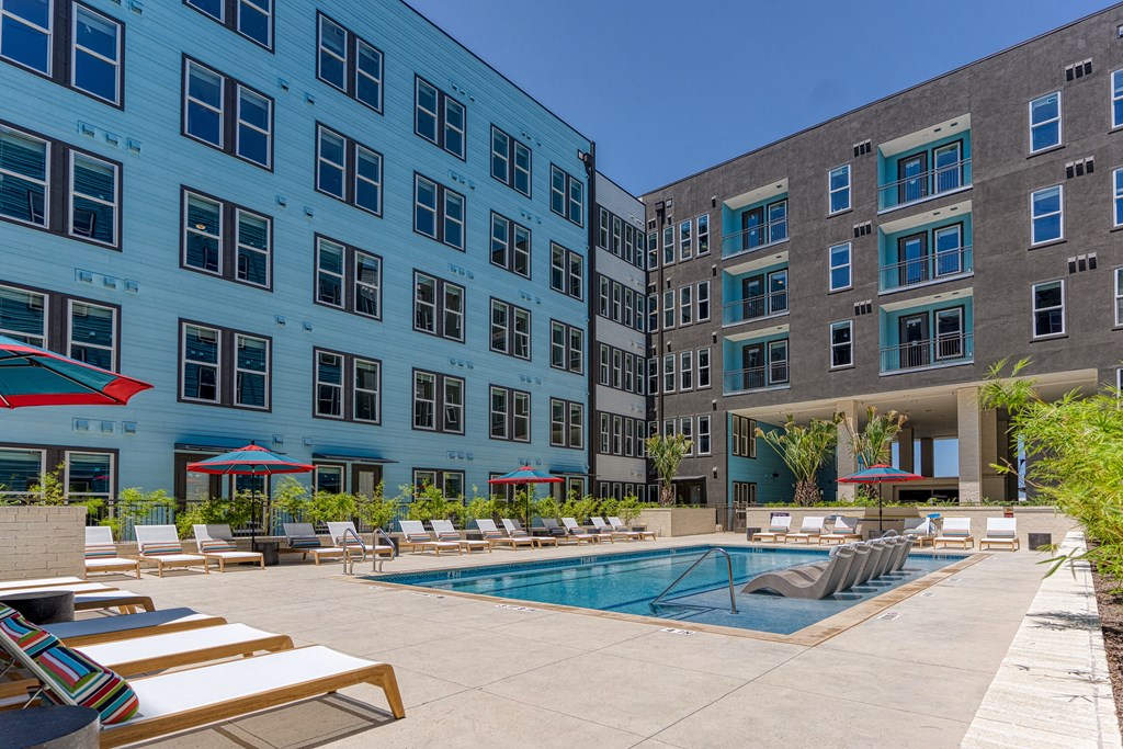 a swimming pool with lounge chairs and umbrellas in front of a building