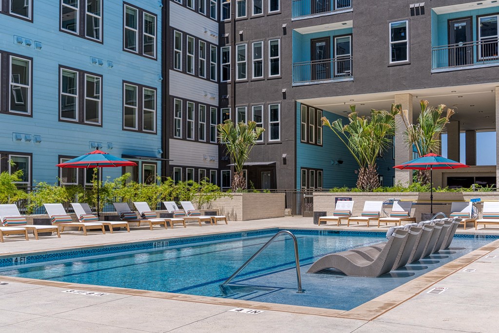a swimming pool with chaise lounge chairs and umbrellas in front of an apartment building