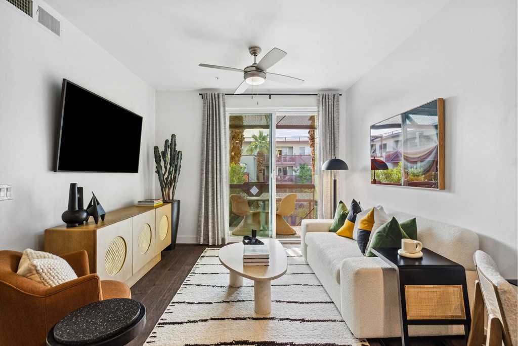 A living room with a white couch, a black table, and a flat screen TV mounted on the wall.