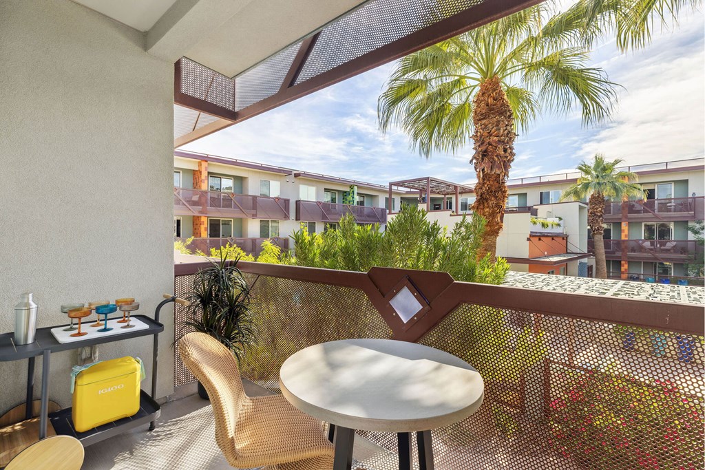 A balcony with a table and chairs overlooking a building with a palm tree.
