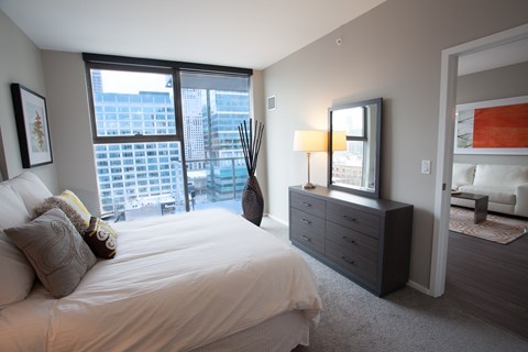 A bedroom with a large bed and a city view through the window.