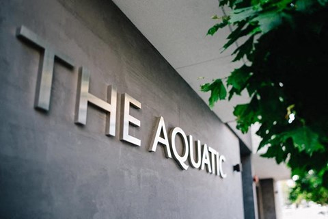 The Aquatic sign on a building with green leaves in the background.