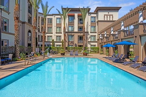 A large swimming pool in front of a hotel with palm trees.