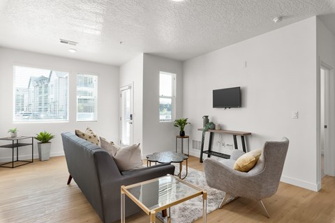 A living room with a grey couch, a glass table, and a television on the wall.